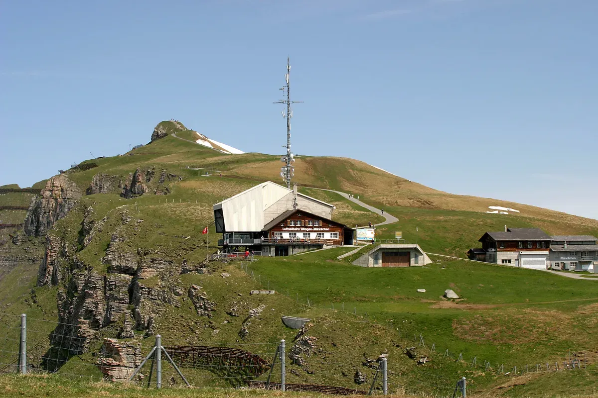The Wengen-Männlichen aerial cableway mountain station on the ridge above Wengen, Switzerland, with the Royal Walk path visible on the summit behind