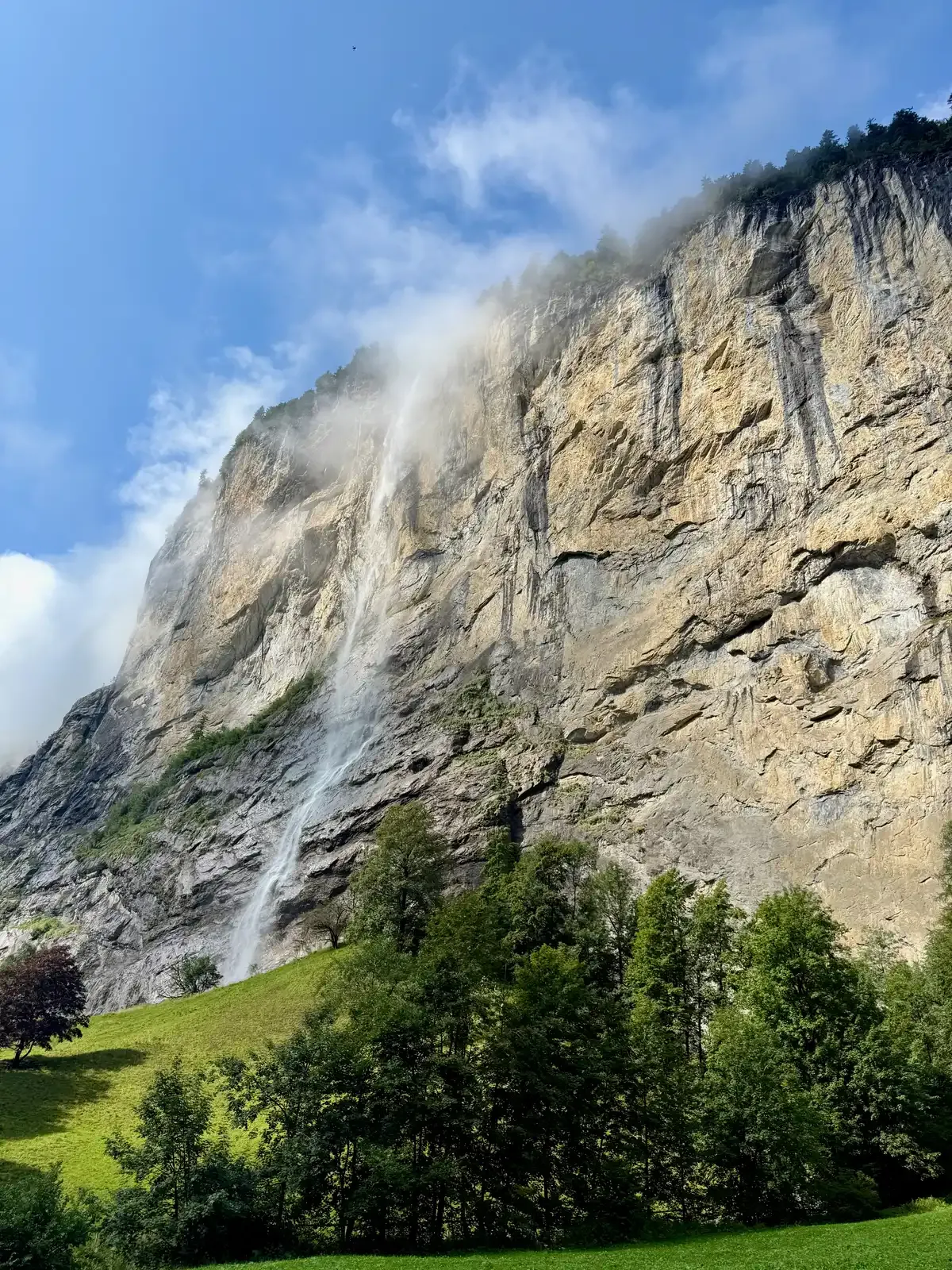 Staubbach Falls dropping off the limestone cliff above the meadows of Lauterbrunnen village, Lauterbrunnen valley, Switzerland